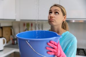  woman holding bucket while water leaking from ceiling in kitchen